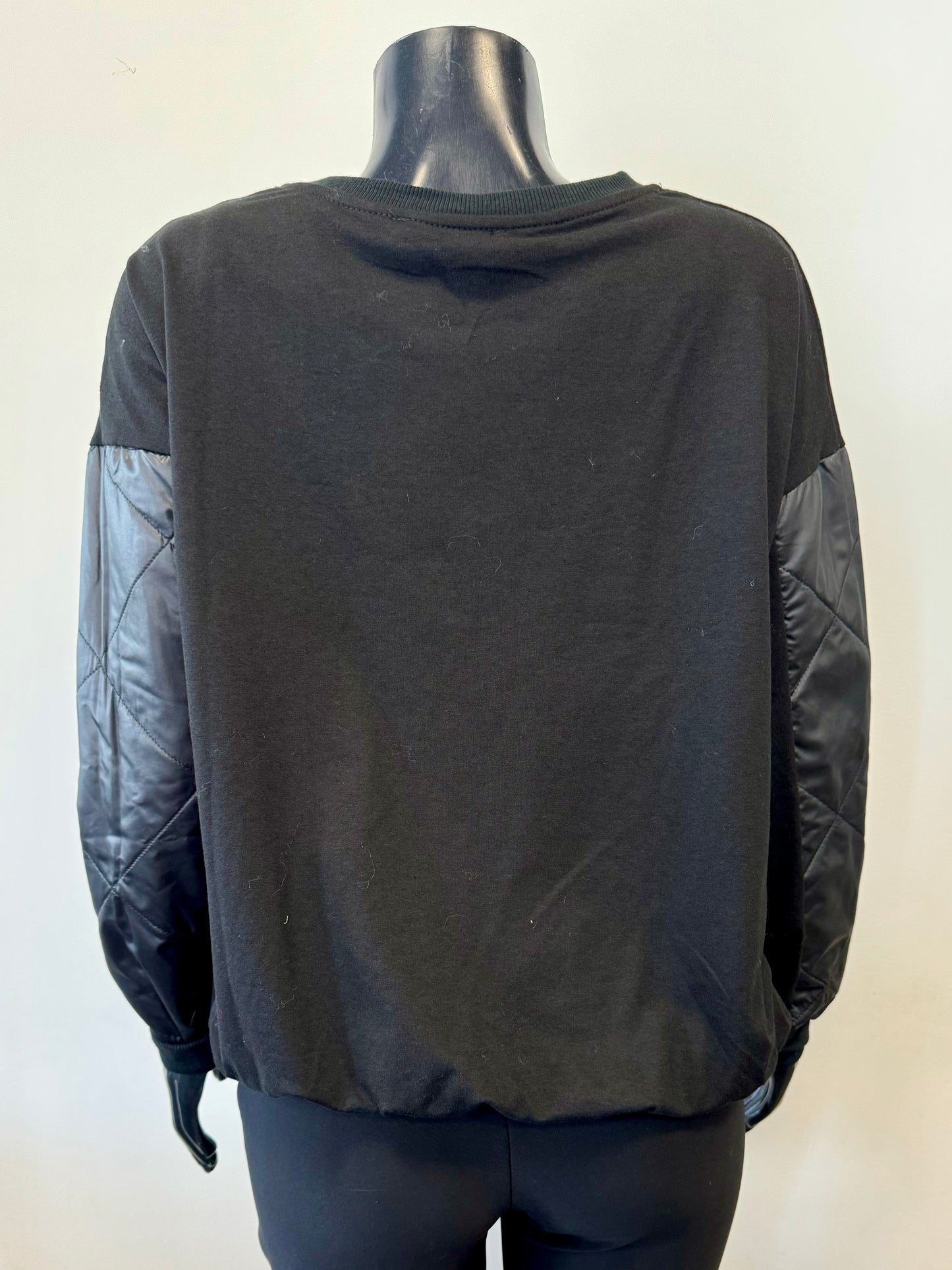 A stylish sweater from ETERNELLE, known as the Sweater with Pocket - ETERNELLE, is elegantly showcased on a black mannequin. The cozy pullover features quilted nylon patches on the sleeves and a large square quilted nylon pocket on the left side of the chest. Its simple, casual design complements the soft and comfortable fabric perfectly.