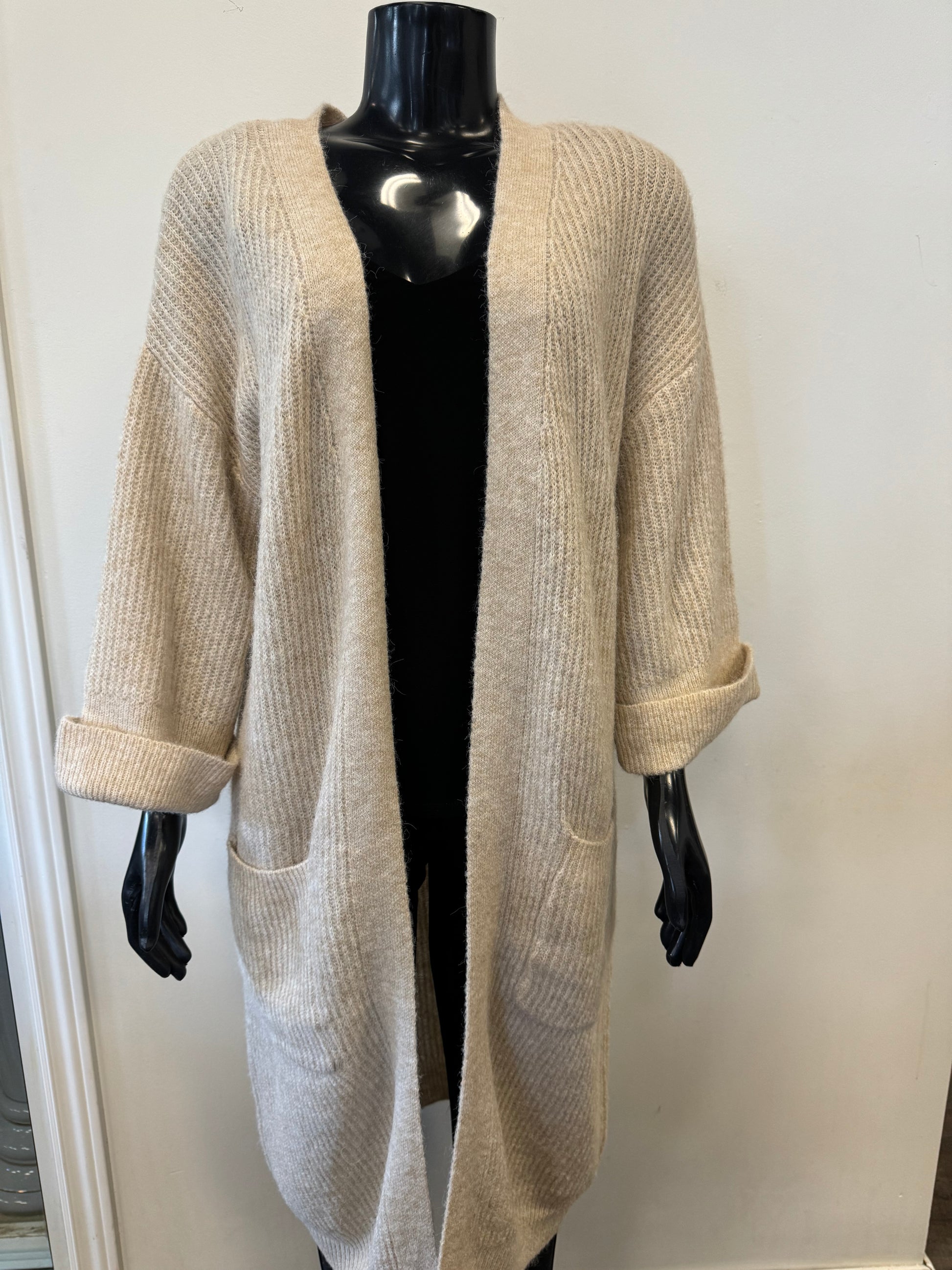 A beige, open-front Cardigan Beige - SoyaConcept by Bali Corp is displayed on a black mannequin. The warm cardigan features ribbed knit fabric, long sleeves with rolled cuffs, and two front pockets. Perfect for layering in cooler weather, the background is a plain, light-colored wall.