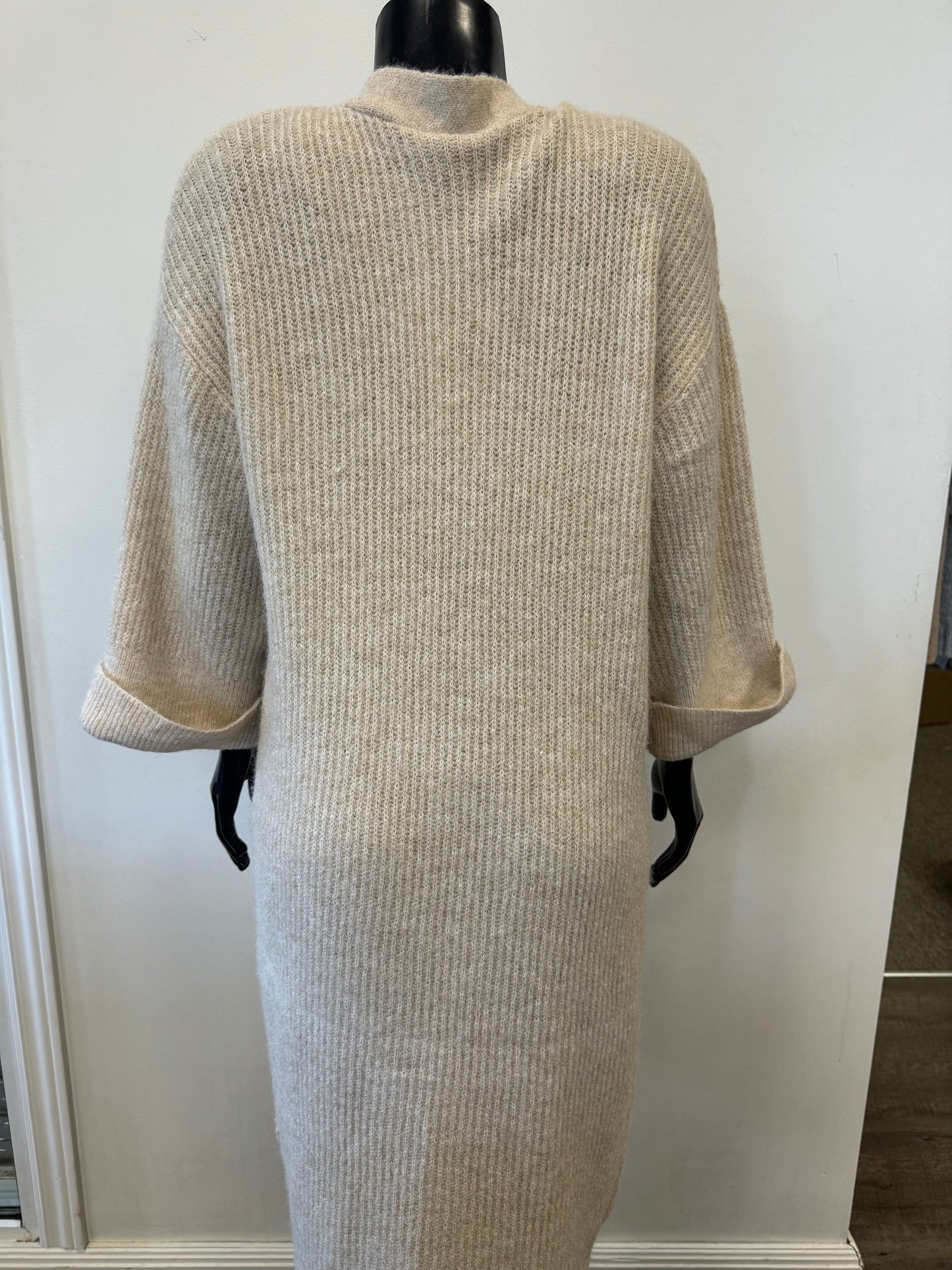 A beige, open-front Cardigan Beige - SoyaConcept by Bali Corp is displayed on a black mannequin. The warm cardigan features ribbed knit fabric, long sleeves with rolled cuffs, and two front pockets. Perfect for layering in cooler weather, the background is a plain, light-colored wall.