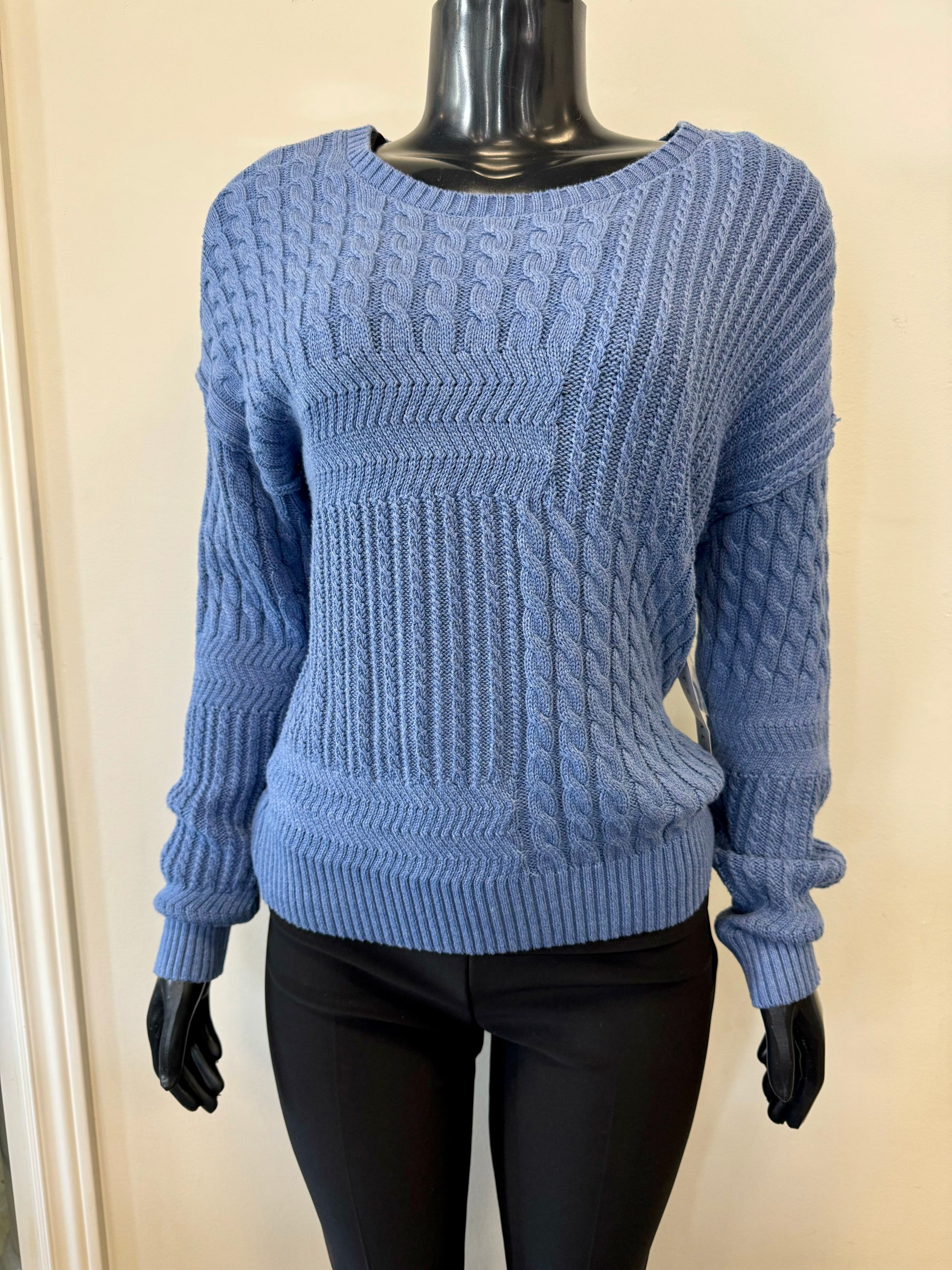 A mannequin dressed in Tribal's blue, long-sleeve Knit Rope Sweater Blue - Tribal H.DENIM, made from 100% cotton and featuring detailed patterns like cables and textured stitches, stands against a beige background, paired with black H.DENIM pants.