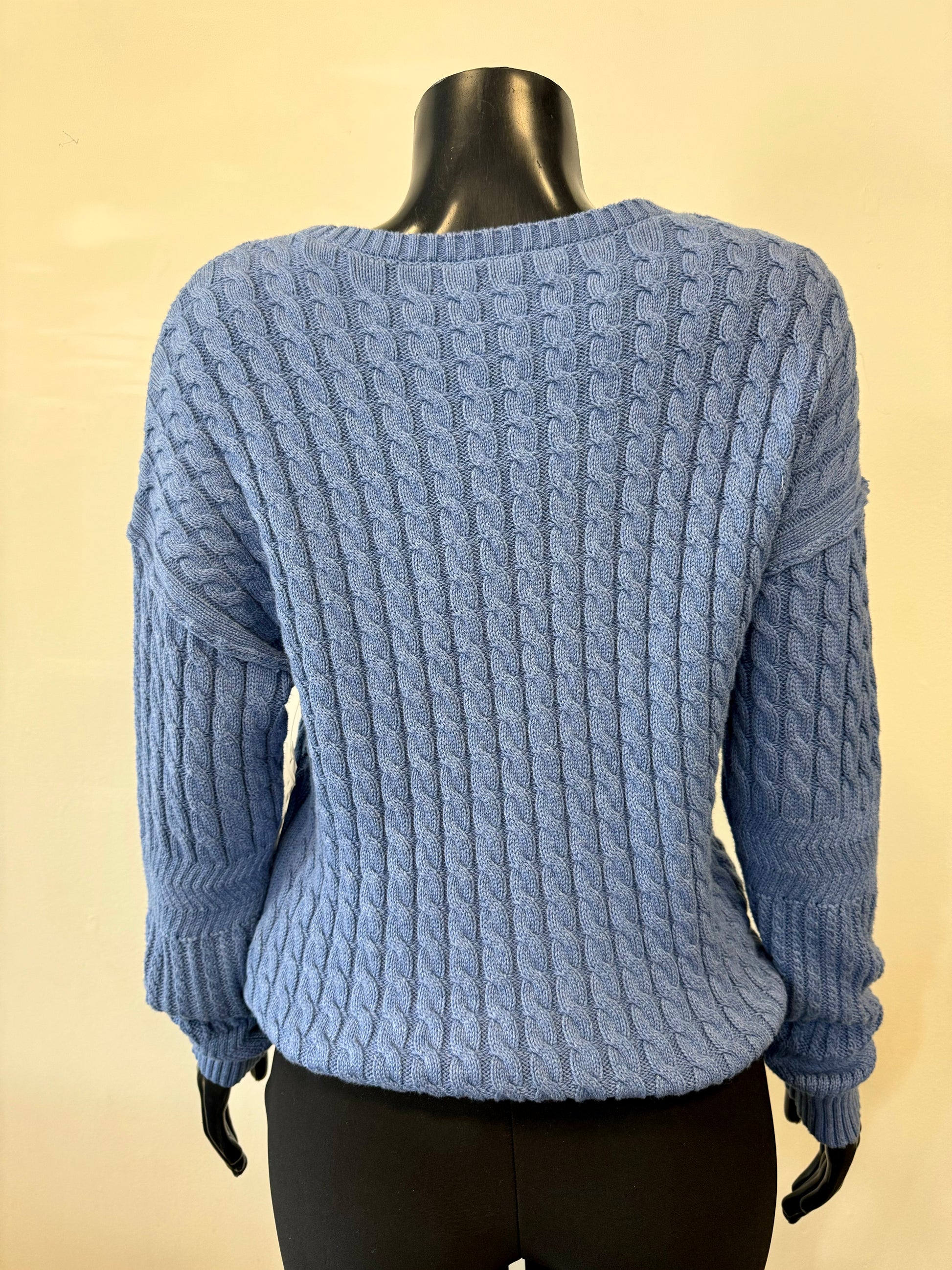 A mannequin dressed in Tribal's blue, long-sleeve Knit Rope Sweater Blue - Tribal H.DENIM, made from 100% cotton and featuring detailed patterns like cables and textured stitches, stands against a beige background, paired with black H.DENIM pants.