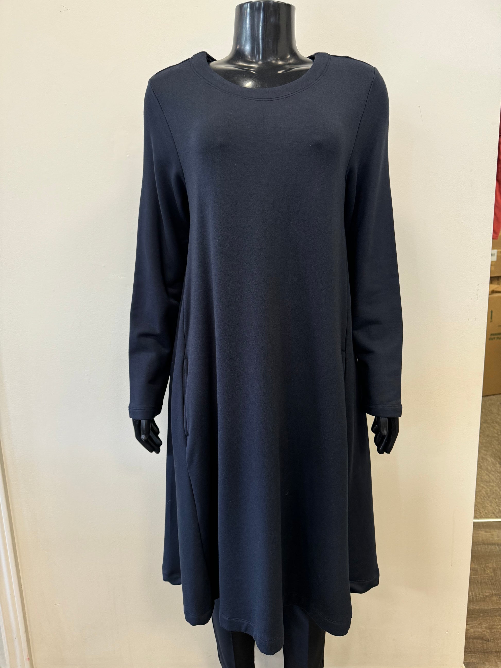 A black mannequin is dressed in the Cosy Up Swing Dress - FOIL FO6681 by FOIL, a long-sleeved, knee-length, navy blue dress made from high-quality viscose. The dress features a round neckline and a relaxed fit, effortlessly blending fashion and functionality. The background is a plain, light-colored wall.