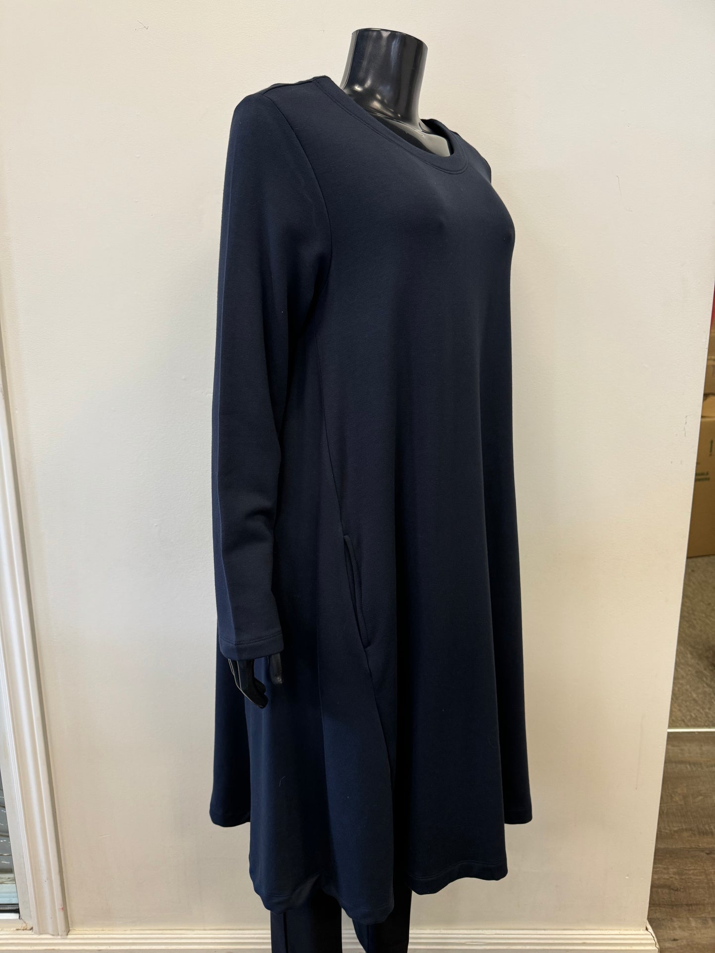 A black mannequin is dressed in the Cosy Up Swing Dress - FOIL FO6681 by FOIL, a long-sleeved, knee-length, navy blue dress made from high-quality viscose. The dress features a round neckline and a relaxed fit, effortlessly blending fashion and functionality. The background is a plain, light-colored wall.