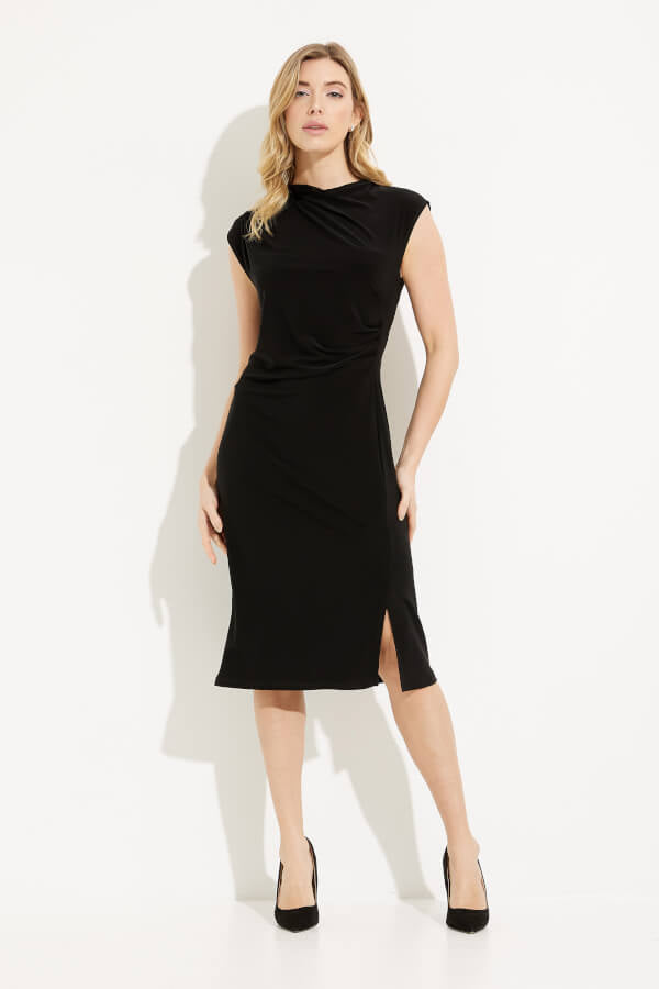 A woman with long, blonde hair stands against a plain white background, wearing the Draped Neck Dress Style 233211 by Joseph Ribkoff. The sleeveless black dress features a draped neckline and a knee-length hem with a small slit on one side. Her left hand touches her chin while her right hand rests on her hip.