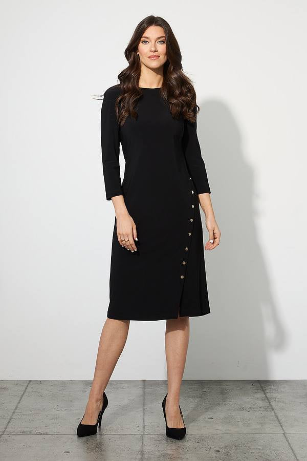 A woman stands against a plain white wall on a concrete floor, wearing the knee-length Rivet Detail Dress Style 223173 by Joseph Ribkoff. The dress features three-quarter sleeves, a plunging neckline, and buttons running down one side. She has long, wavy hair and wears black high heels. MADE IN CANADA marks the quality of her elegant attire from Joseph Ribkoff.