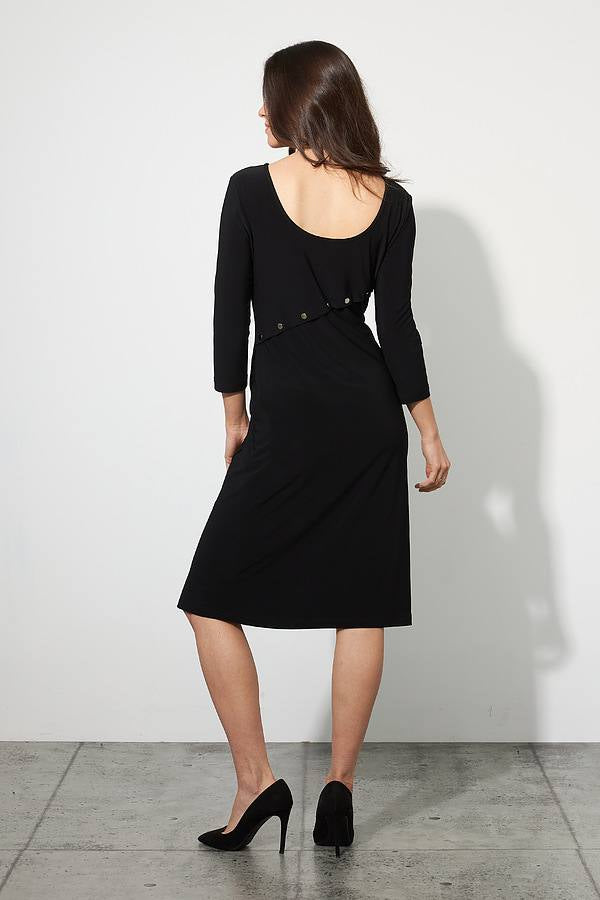 A woman stands against a plain white wall on a concrete floor, wearing the knee-length Rivet Detail Dress Style 223173 by Joseph Ribkoff. The dress features three-quarter sleeves, a plunging neckline, and buttons running down one side. She has long, wavy hair and wears black high heels. MADE IN CANADA marks the quality of her elegant attire from Joseph Ribkoff.