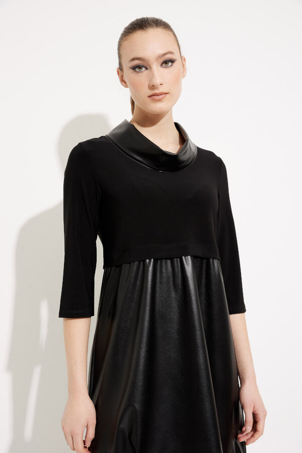 A woman stands against a white background wearing the Joseph Ribkoff Faux Leather Cocoon Dress Style 233091, a black empire waist dress with three-quarter sleeves and a shiny faux-leather material on the lower portion. She pairs the dress with knee-high black boots and has her hair styled in a neat updo.