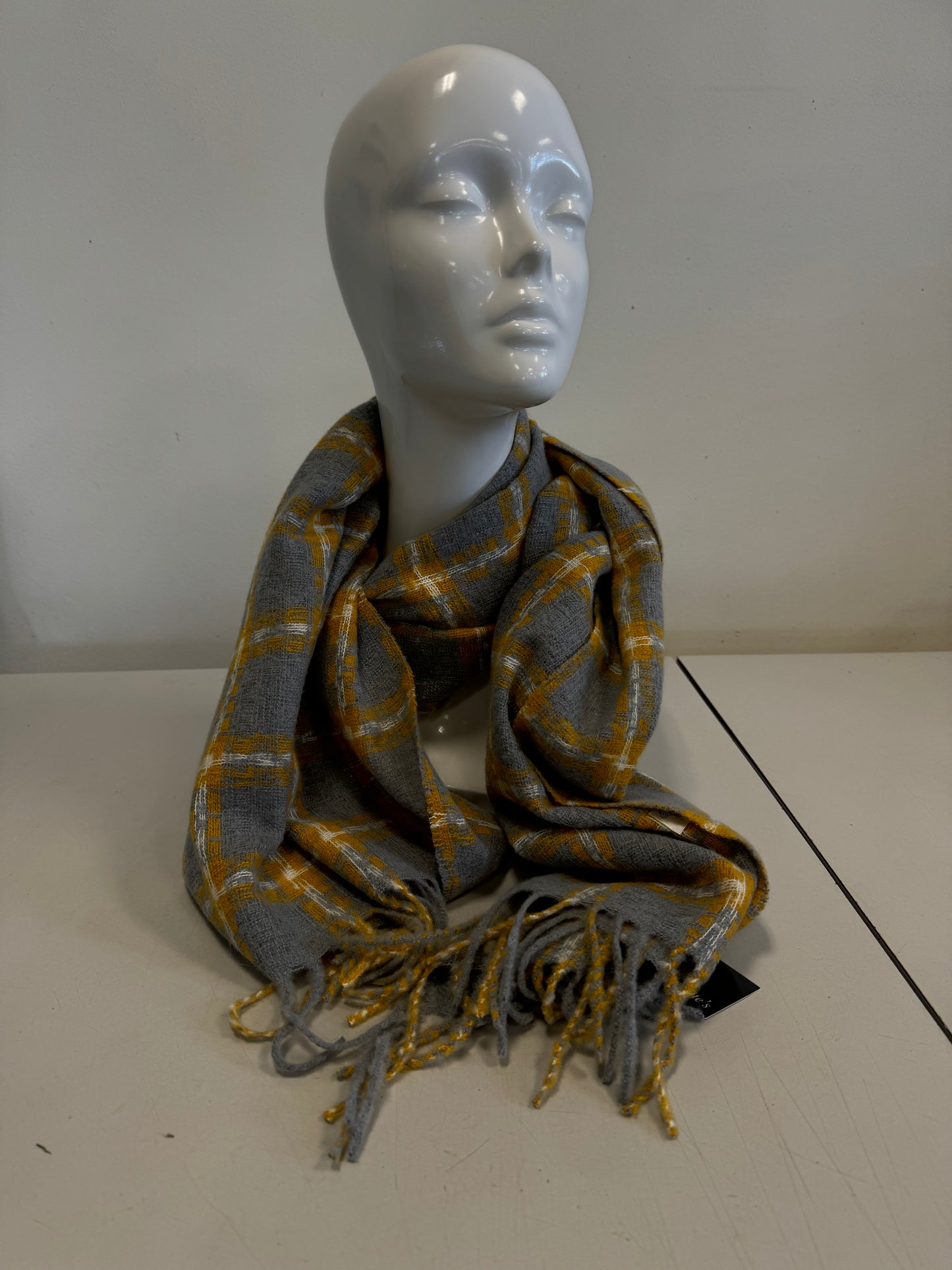 A chic Yellow and Grey Plaid Scarf with fringed ends from Catherine Lillywhite is elegantly draped around a white mannequin head and neck, set against a plain white background on a light-colored surface.