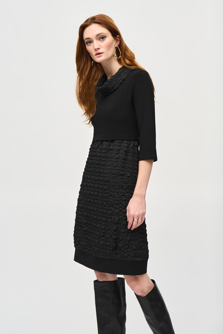 A woman with long red hair is wearing the Jacquard And Silky Knit Cocoon Dress 243114 by Joseph Ribkoff, featuring three-quarter sleeves and a textured skirt. She has one hand in her pocket and is standing against a plain white background, also accessorized with large hoop earrings.