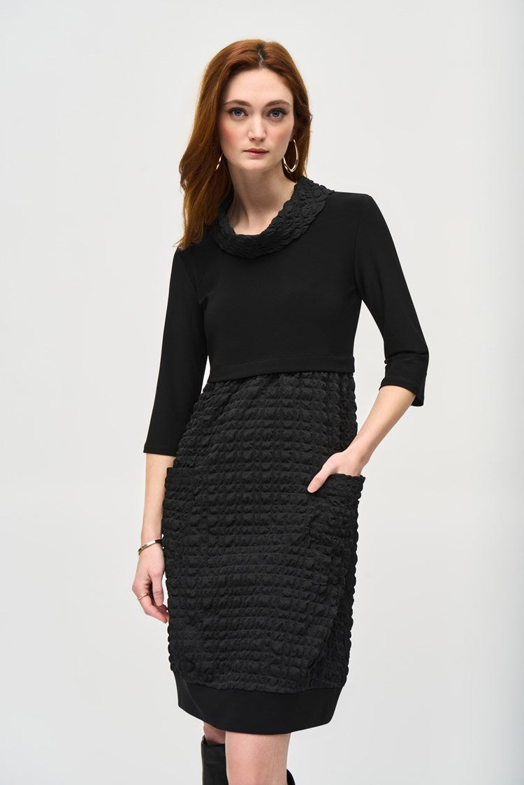 A woman with long red hair is wearing the Jacquard And Silky Knit Cocoon Dress 243114 by Joseph Ribkoff, featuring three-quarter sleeves and a textured skirt. She has one hand in her pocket and is standing against a plain white background, also accessorized with large hoop earrings.