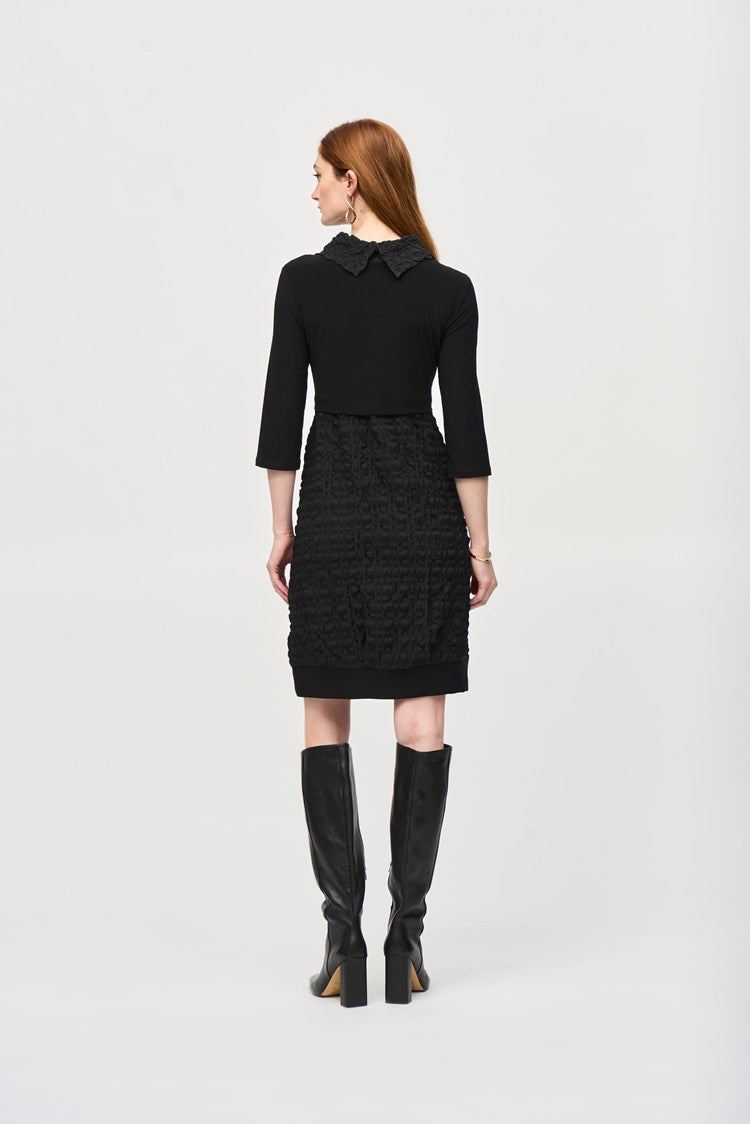 A woman with long red hair is wearing the Jacquard And Silky Knit Cocoon Dress 243114 by Joseph Ribkoff, featuring three-quarter sleeves and a textured skirt. She has one hand in her pocket and is standing against a plain white background, also accessorized with large hoop earrings.