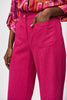A person is shown wearing Joseph Ribkoff's Corduroy Culotte Pant 243295 in a vibrant pink jacquard pattern, featuring visible front pockets and a button closure. The top appears to be a colorful blouse with shades of pink, orange, and white. One hand is casually placed into a pocket.
