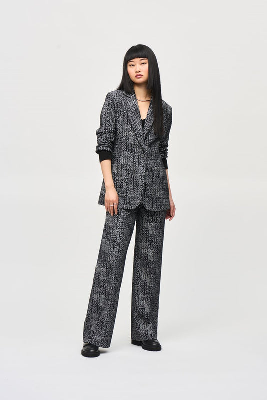 A person with long, straight black hair and bangs stands against a plain background. They are wearing a black and white patterned tweed knit fabric blazer with matching wide-leg pants, specifically Tweed Knit Wide-Leg Pull-On Pants 243288 by Joseph Ribkoff, and black shoes. They have an expressionless face, and their hands are relaxed by their sides.