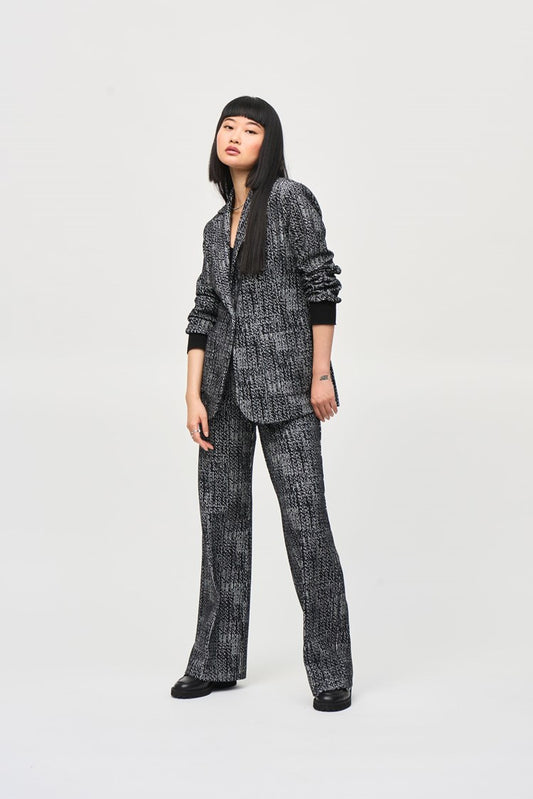 A person with long, straight hair stands against a plain backdrop wearing a matching dark patterned Joseph Ribkoff Tweed Knit Fitted Blazer (243053) and wide-leg pants with a textured design, embodying the elegance of a versatile fashion piece. Their hands are relaxed at their sides as they look slightly to the left with a neutral expression.