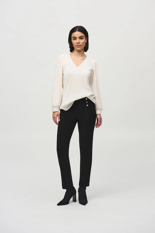 Against a plain background, a person with shoulder-length hair is posing in a long-sleeve, white Pleated Knit Boxy V-Neck Top 244163 by Joseph Ribkoff, which features stylish puff sleeves. They pair the blouse with black trousers and complete the look with black ankle boots. Looking directly at the camera with their arms relaxed by their sides, they exude a casual-chic style.