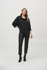 A woman stands against a plain white background, wearing a black Woven Jacquard Boxy Top 244069 by Joseph Ribkoff with three-quarter sleeves, black leather pants with side pockets, and black heeled ankle boots. Her left hand is on her hip and her right arm hangs by her side. She has long, wavy hair.
