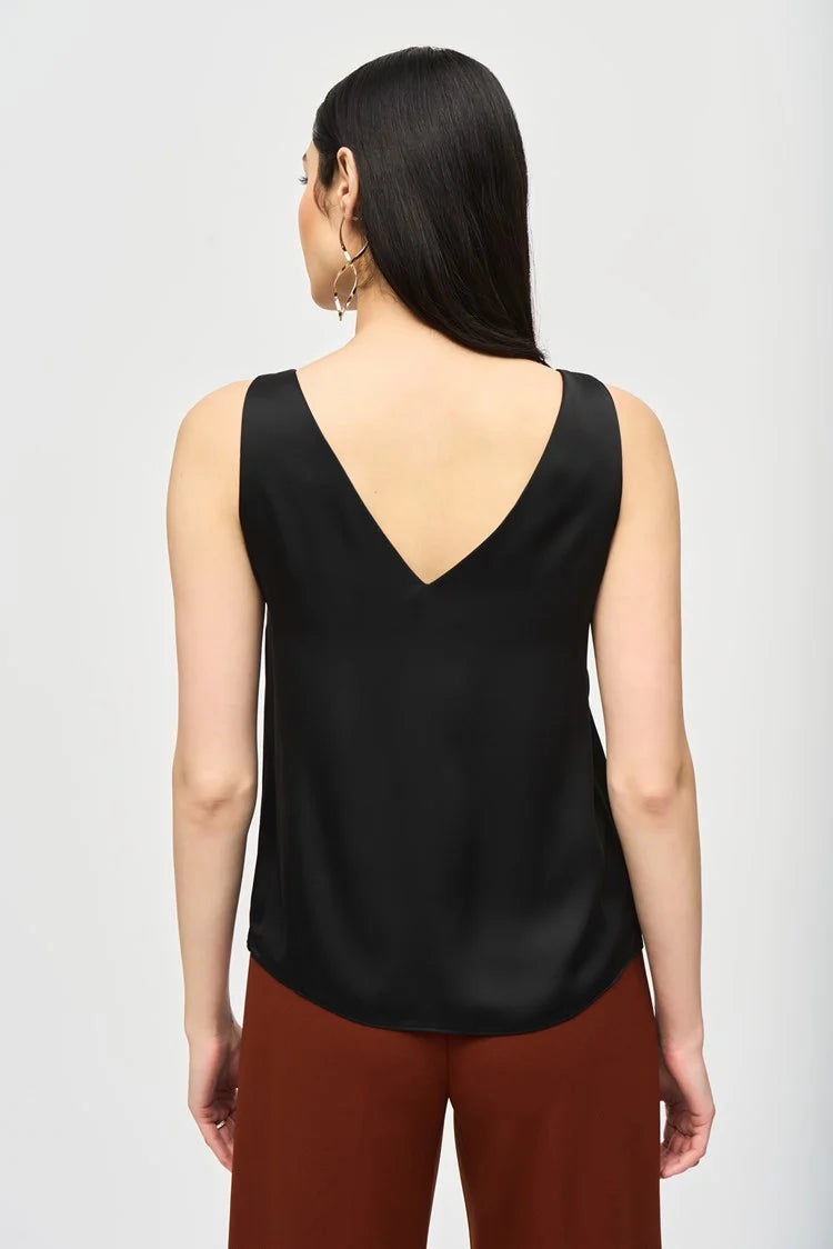 A woman with long, dark hair is wearing a Joseph Ribkoff Satin Straight Sleeveless Top 243110, which features a V-shaped neckline, paired with brown pants. She stands against a plain white background and has a neutral expression. She is also adorned with long, dangling earrings.