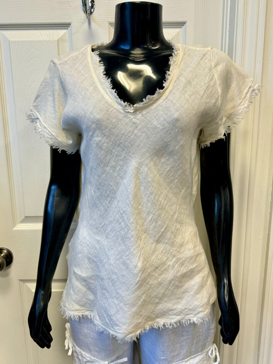 A mannequin showcases the LINEN TOP VANILLA- ETERNELLE by ETERNELLE, featuring a light beige, short-sleeved, V-neck design with frayed edges. The 100% linen fabric has a textured, woven appearance. The vanilla-hued top is paired with matching pants and displayed against a white-paneled door background.