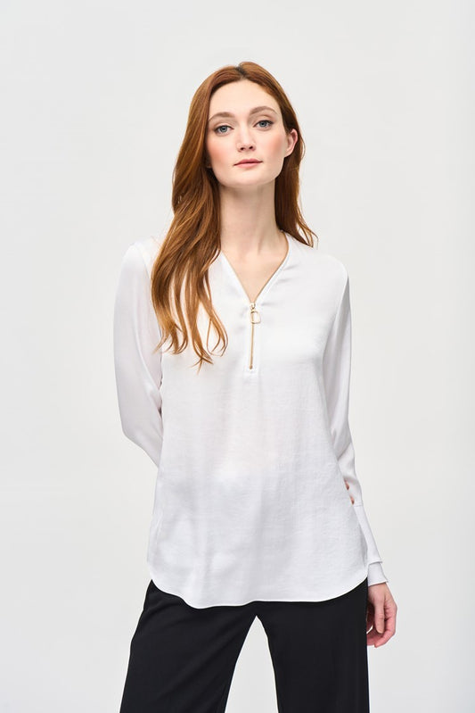 A woman with long reddish-brown hair wearing the Joseph Ribkoff Satin Boxy Top With Ruffled Sleeve 243285, which features a V-shaped neckline and long ruffled sleeves, stands against a plain white background. She is looking directly at the camera with a neutral expression, one hand by her side and the other resting on her hip.