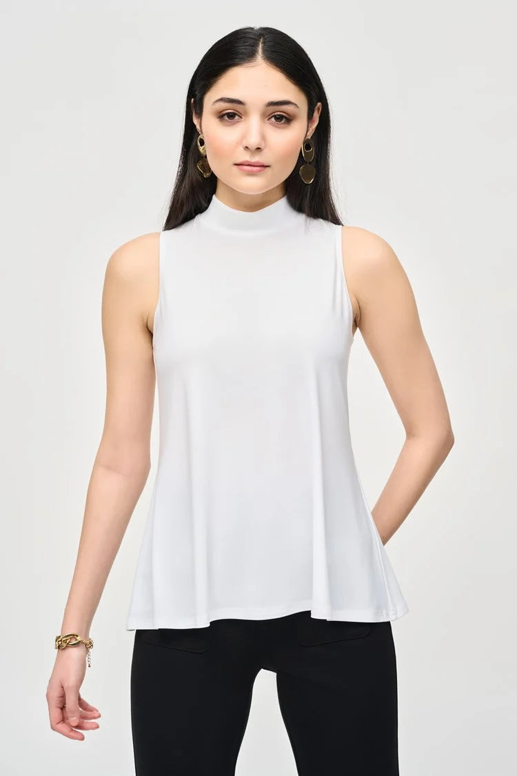 A woman with long dark hair stands against a plain background. She is wearing a Joseph Ribkoff Silky Knit Fit and Flare Sleeveless Top 243253, black flared pants, and black ankle boots. She has minimal jewelry and is striking a relaxed, confident pose with a slight smile.