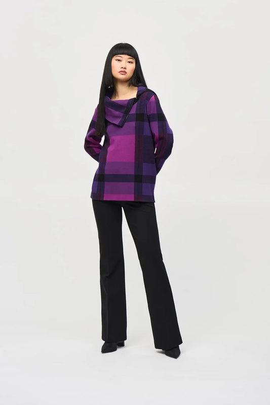 A person with straight, long dark hair and full bangs wears the Plaid Jacquard Cowl Neck Sweater 243943 by Joseph Ribkoff, showcasing its purple and black checkered design, along with black pants. The individual stands confidently against a plain white background.