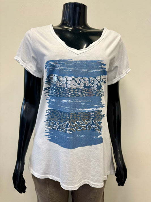 A black mannequin is adorned in an elegant Femme Fatale Blue Paintstroke Tee (FEMME FATALE T-32TEE) featuring a white V-neck and blue, horizontally striped abstract pattern on the front. Complemented by beige pants, this outfit exudes Italian elegance against the backdrop of a plain light-colored wall.