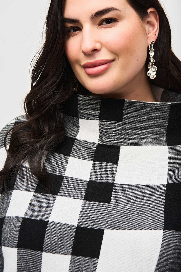 A woman is dressed in the Joseph Ribkoff Plaid Jacquard Knit Sweater 243946 and a matching skirt with leatherette trim. She is standing against a plain white background, wearing black heeled boots and accessorized with earrings and a bracelet. She has long dark hair and is posing confidently.