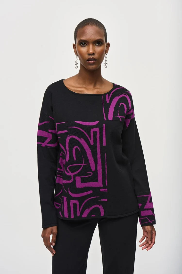 A person stands confidently against a white background wearing a stylish Jacquard Knit Abstract Print Top 243971 by Joseph Ribkoff. They are dressed in a black long-sleeve top featuring vibrant purple geometric patterns on one side and black flared pants. The cozy fabric drapes beautifully as they pose with one hand on their hip.