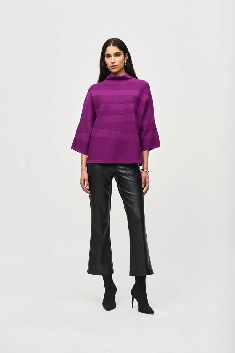 A person with short, tousled blonde hair is wearing a radiant purple *Sweater Knit Mock Neck Boxy Top 243953* by Joseph Ribkoff, which features elegant bell sleeves and horizontal patterns. They rest their arm across the shoulder of another person who is partially visible on the left side of the image under a blurred background of city buildings.