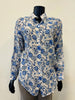 A mannequin dressed in a long-sleeve "Allover Print Blouse - FEMME FATALE T-24B" by Femme Fatale, featuring a blue and white floral pattern, exudes a luxurious feel. The blouse is paired with gray pants, creating an effortlessly chic look. The mannequin is set against a plain, light-colored background.