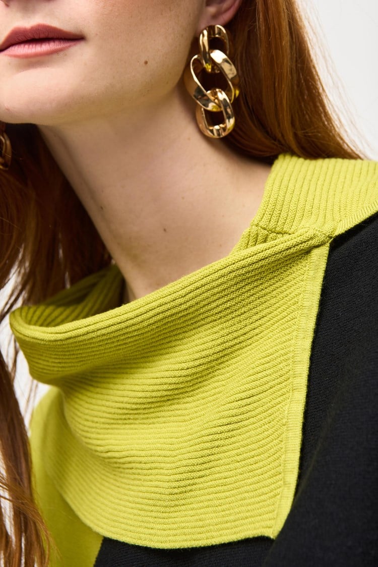 A woman with long red hair stands against a plain background, wearing the Color-Block Jacquard Sweater Top 243941 by Joseph Ribkoff. The cozy fashion sweater in black, gray, and lime green features a unique geometric design with an asymmetrical neckline. She has one hand resting on her hip and is looking to the side.