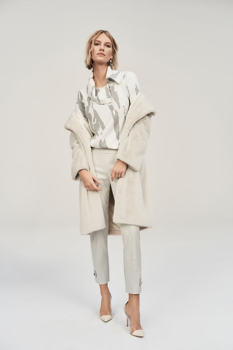 A person is wearing a stylish beige coat over the Joseph Ribkoff Jacquard Sweater Knit Cowl Neck Top 243945, paired with checked pants. They are also sporting white high heels. The background is a plain light color, focusing entirely on the fashionable outfit.