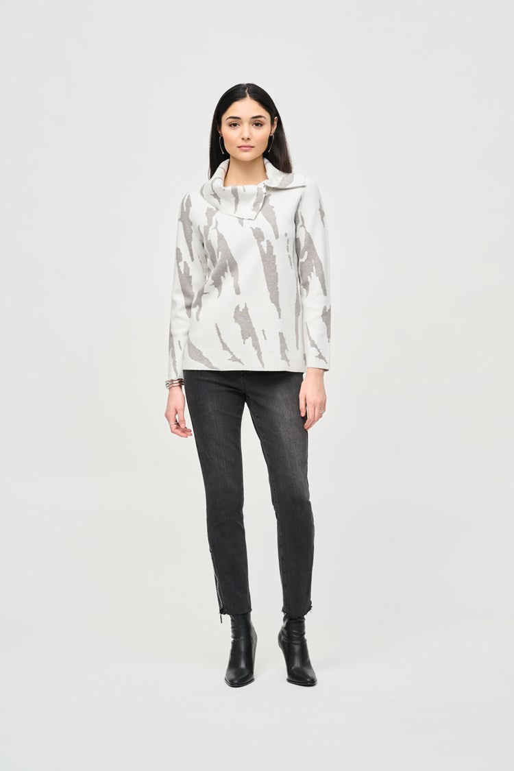 A person is wearing a stylish beige coat over the Joseph Ribkoff Jacquard Sweater Knit Cowl Neck Top 243945, paired with checked pants. They are also sporting white high heels. The background is a plain light color, focusing entirely on the fashionable outfit.