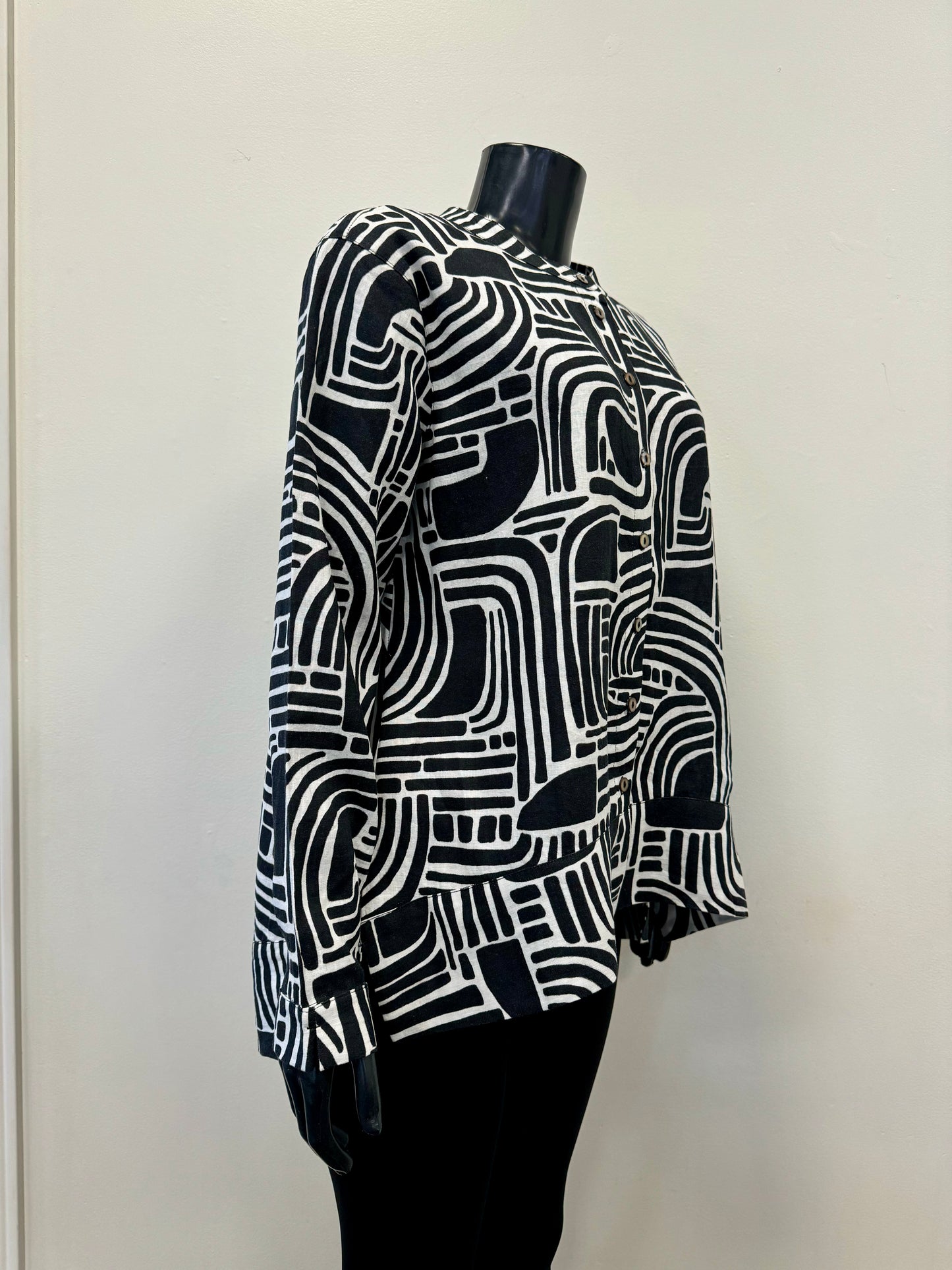 A mannequin sporting the FOIL Summer Days Linen Shirt - FOIL FO7463, showcasing a striking abstract geometric pattern. This black and white long-sleeve button-up, crafted from premium linen, features a labyrinth-like design of curved and straight lines with white buttons down the front. Ideal for your summer wardrobe, it makes a statement against a plain background.