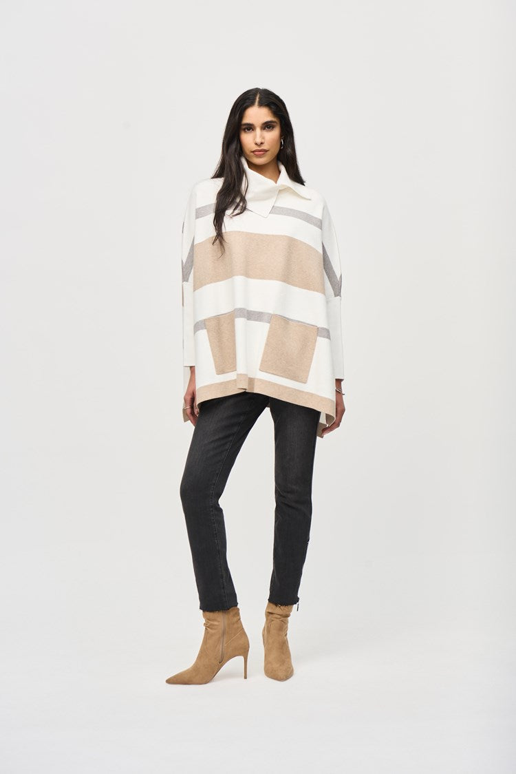 A woman with long dark hair is wearing the Joseph Ribkoff Jacquard Sweater Knit Poncho 243951, a loose-fitting, beige and white striped poncho-style top with a cowl neckline. She pairs it with black skinny jeans and tan suede ankle boots. She stands against a plain white background in a relaxed posture, looking directly at the camera.