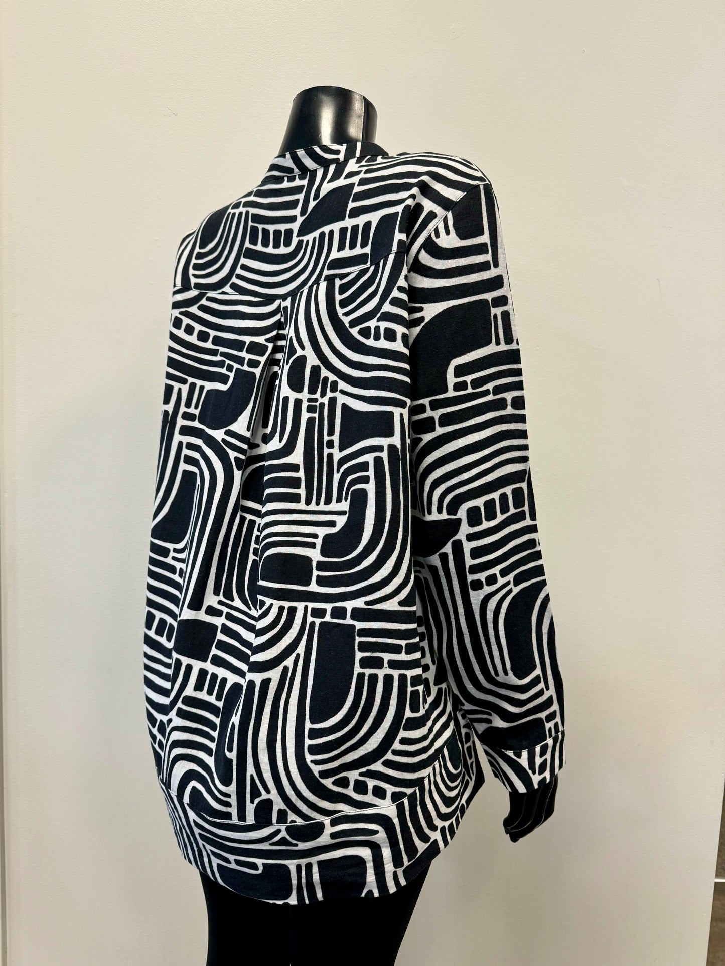 A mannequin sporting the FOIL Summer Days Linen Shirt - FOIL FO7463, showcasing a striking abstract geometric pattern. This black and white long-sleeve button-up, crafted from premium linen, features a labyrinth-like design of curved and straight lines with white buttons down the front. Ideal for your summer wardrobe, it makes a statement against a plain background.