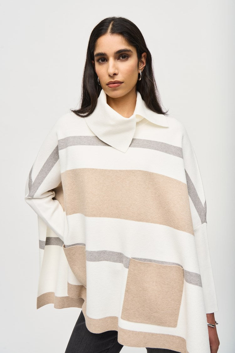 A woman with long dark hair is wearing the Joseph Ribkoff Jacquard Sweater Knit Poncho 243951, a loose-fitting, beige and white striped poncho-style top with a cowl neckline. She pairs it with black skinny jeans and tan suede ankle boots. She stands against a plain white background in a relaxed posture, looking directly at the camera.