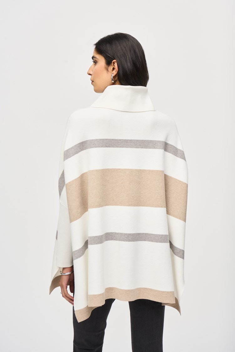 A woman with long dark hair is wearing the Joseph Ribkoff Jacquard Sweater Knit Poncho 243951, a loose-fitting, beige and white striped poncho-style top with a cowl neckline. She pairs it with black skinny jeans and tan suede ankle boots. She stands against a plain white background in a relaxed posture, looking directly at the camera.