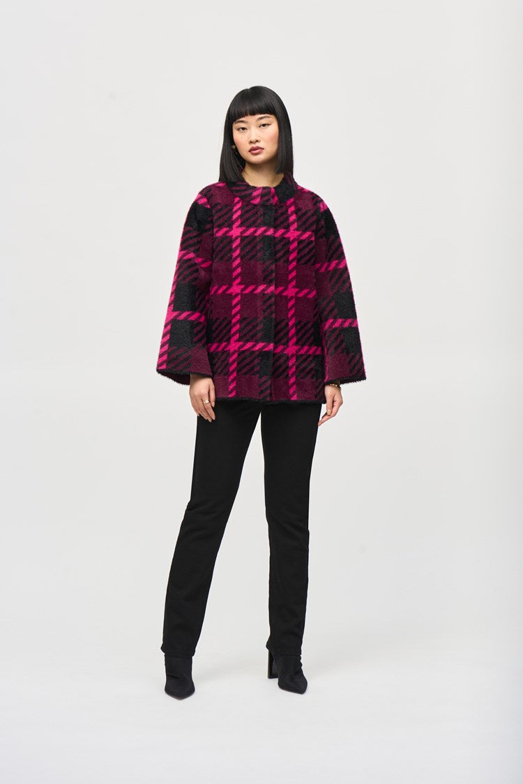 A woman with straight, shoulder-length black hair poses in a vibrant pink and black Feather Yarn Jacquard Plaid Jacket (style number 243931) by Joseph Ribkoff, featuring a funnel collar. She pairs it with black pants and ankle boots. She stands against a plain white background, facing forward with a neutral expression.