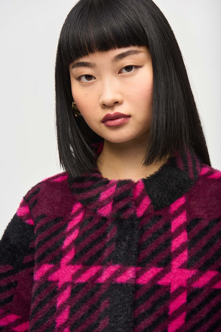 A woman with straight black hair and bangs stands against a plain background. She is wearing the stylish Feather Yarn Jacquard Plaid Jacket 243931 by Joseph Ribkoff, featuring a bold magenta and black checkered pattern. She has a neutral expression, and her arms are relaxed at her sides.