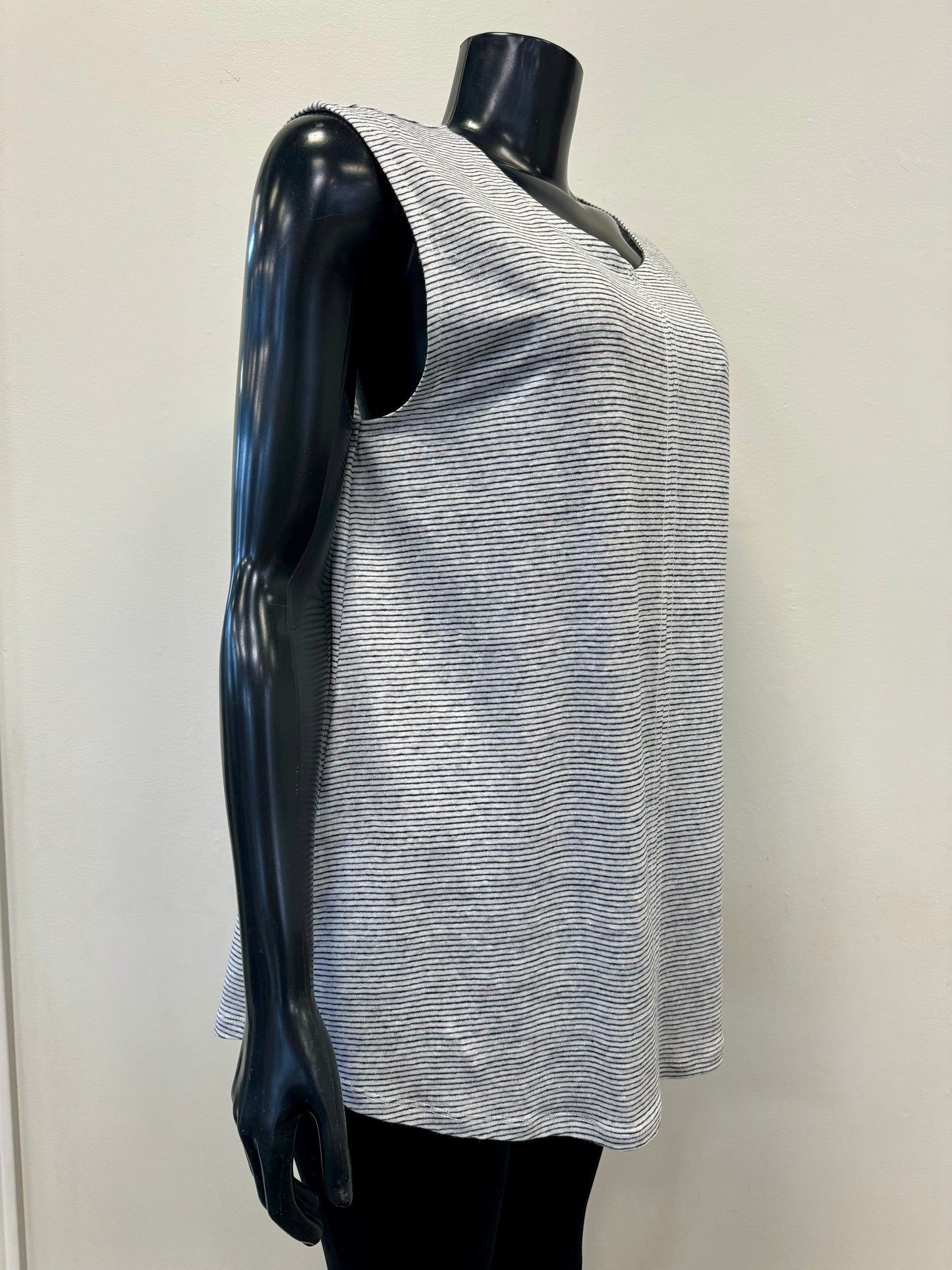 A black mannequin displays the Seams Great Top - FOIL CFO7404, a sleeveless, lightweight blouse from the brand FOIL. The gray and white striped blouse is made from 100% linen, featuring a round neckline and a slightly curved hem. The backdrop is plain and off-white.