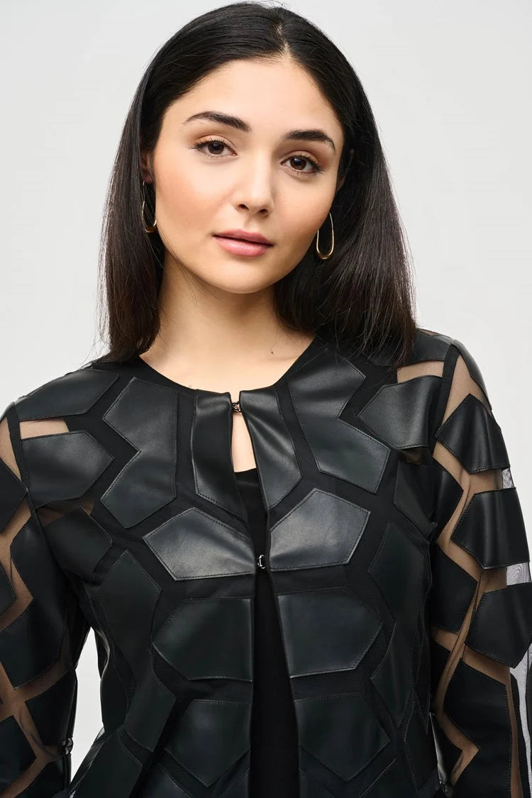 A woman with curly hair stands against a plain white background. She is wearing a white top with a bold black geometric pattern, black pants, and sleek black high-heeled sandals. Draped over her shoulders is the Joseph Ribkoff Laser-Cut Leatherette on Mesh Jacket 241905, enhancing her confident and professional demeanor with a contemporary aesthetic.