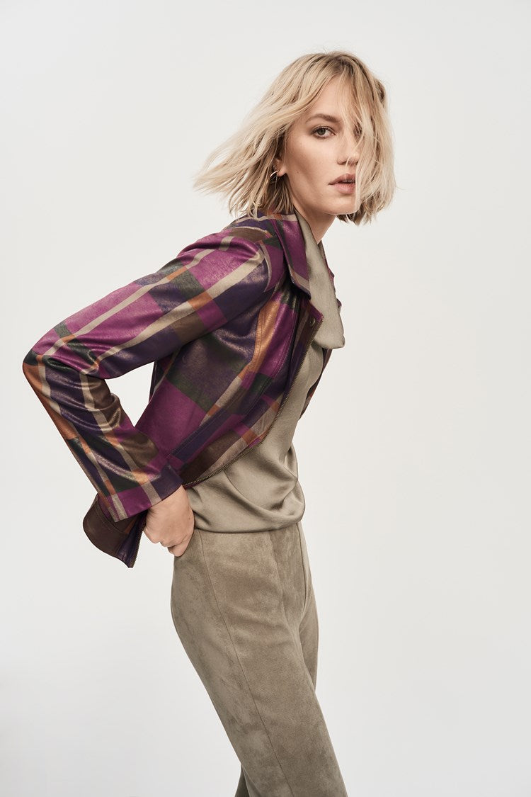 A person with shoulder-length blonde hair is leaning forward slightly while wearing the Foiled Print Faux Suede Jacket 243921 by Joseph Ribkoff over a light-colored top and taupe pants. The background is plain and light-colored, emphasizing the outfit and pose.