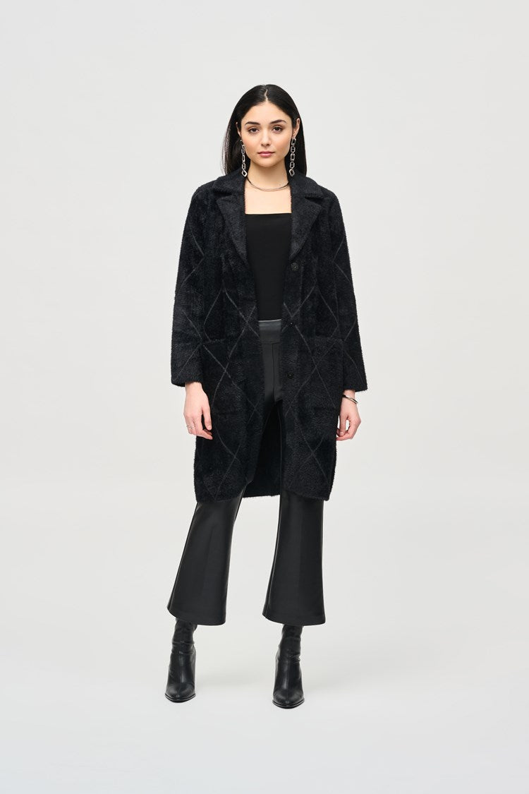 A person stands against a light gray background, wearing the Joseph Ribkoff Notched Collar Coat (style 233951F24) in black over a black top and black pants. They also have on black heeled ankle boots and large, dangling earrings. Their hands are relaxed at their sides.