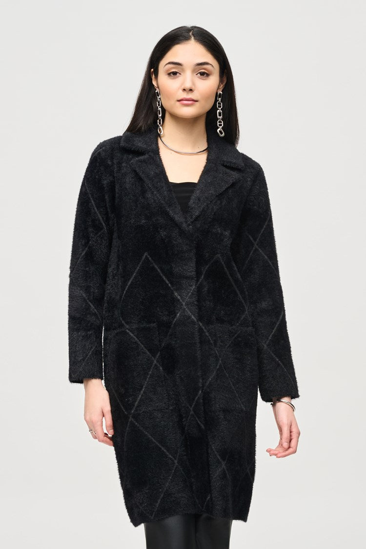 A person stands against a light gray background, wearing the Joseph Ribkoff Notched Collar Coat (style 233951F24) in black over a black top and black pants. They also have on black heeled ankle boots and large, dangling earrings. Their hands are relaxed at their sides.