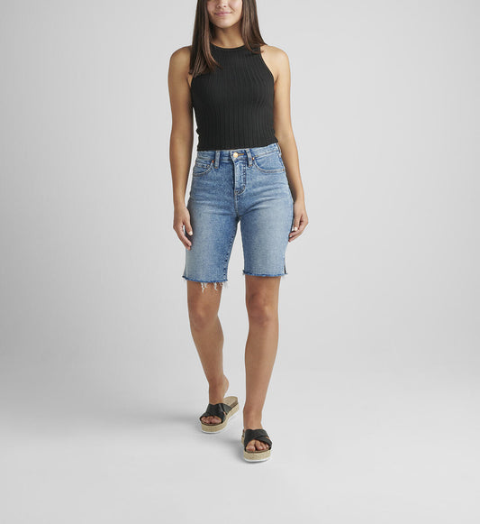 A person stands against a plain background, wearing a black sleeveless ribbed top and light blue City High Rise Shorts by JAG made from Power Stretch Denim with a frayed hem. They wear black platform sandals and have straight, long hair falling loose. Their right arm is relaxed by their side while the left arm is slightly bent.