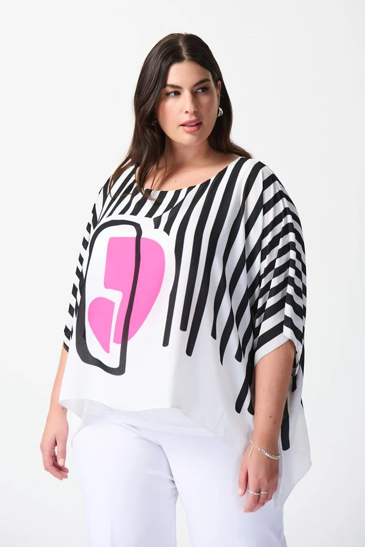 A woman stands confidently against a plain white background. She is wearing a stylish outfit consisting of the Abstract Print Georgette Poncho Top 241091 by Joseph Ribkoff, featuring black and white stripes with an abstract pink geometric design in the center, paired with white wide-leg pants. She completes the look with white heels.