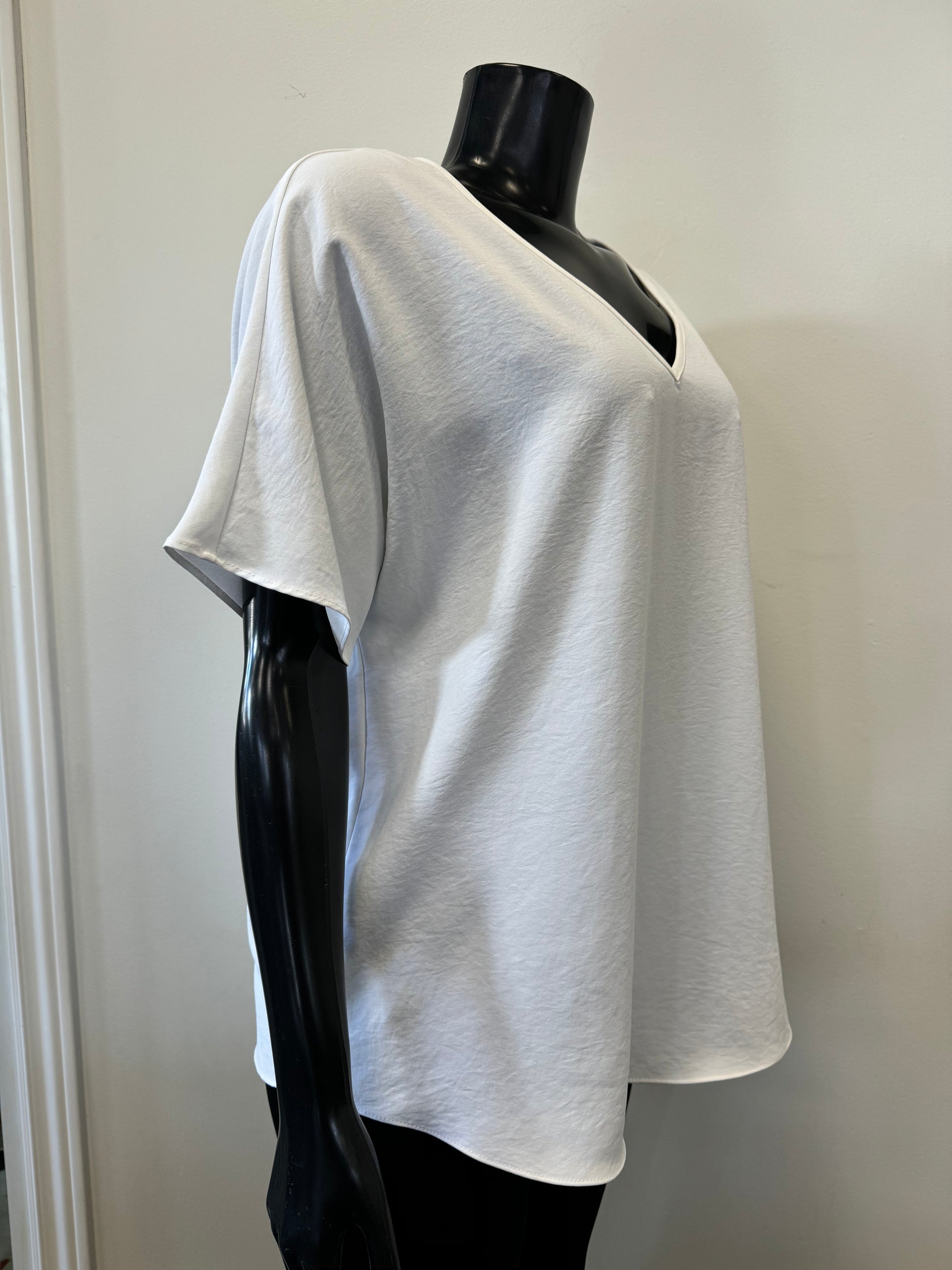 A black mannequin showcases a simple, loose-fitting white V-neck T-shirt with short sleeves and a relaxed fit, known as the Loose V-neck Top Style 231002 by Joseph Ribkoff. The slouchy top is set against a plain, light-colored background.