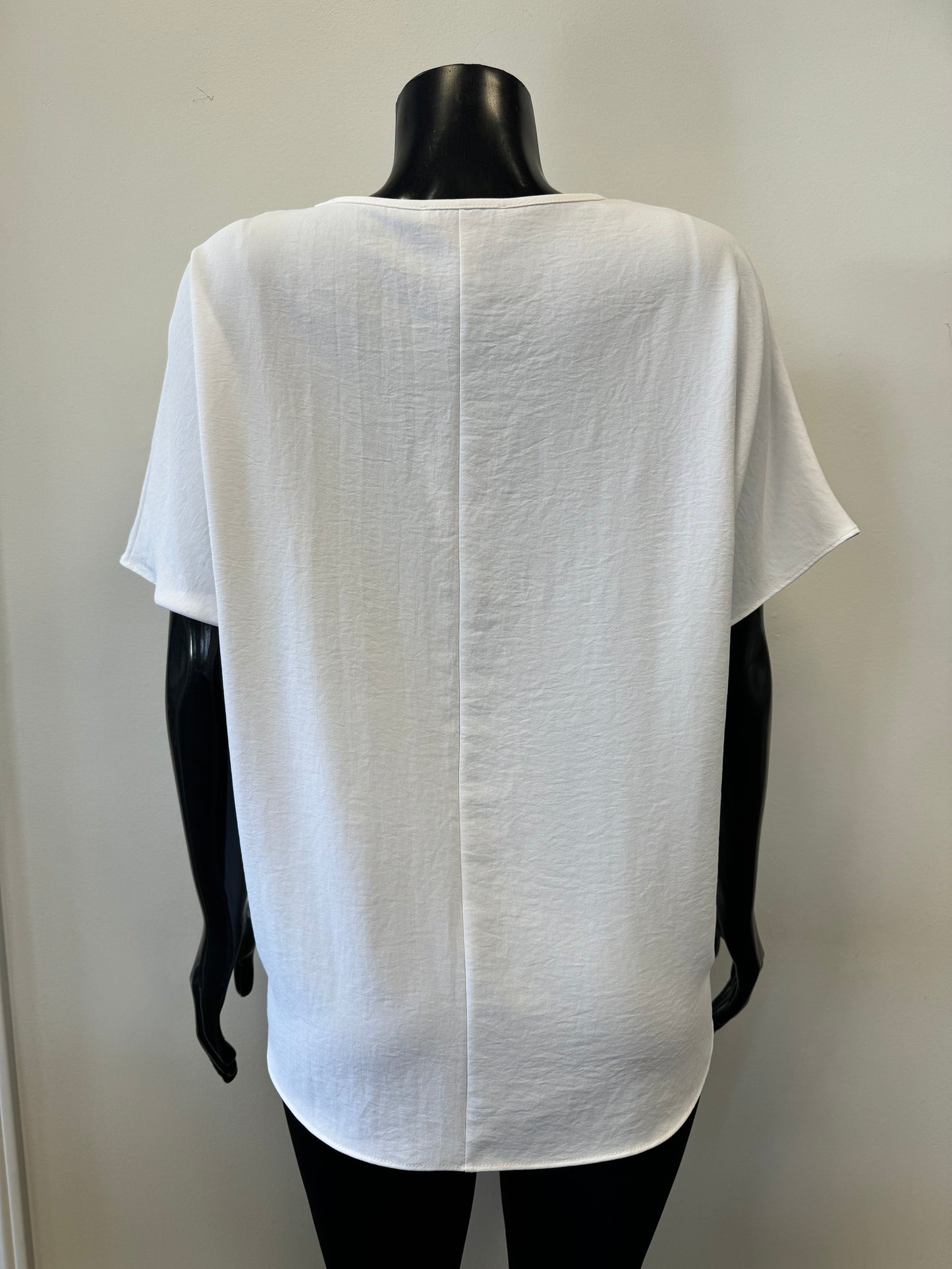 A black mannequin showcases a simple, loose-fitting white V-neck T-shirt with short sleeves and a relaxed fit, known as the Loose V-neck Top Style 231002 by Joseph Ribkoff. The slouchy top is set against a plain, light-colored background.