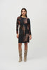 A woman with long dark hair stands against a plain background, wearing the Joseph Ribkoff Sweater Knit Abstract Print Dress 244123. This long-sleeve dress features an abstract print in black, brown, and beige tones. She pairs it with knee-high suede beige boots and has a neutral facial expression and relaxed posture.